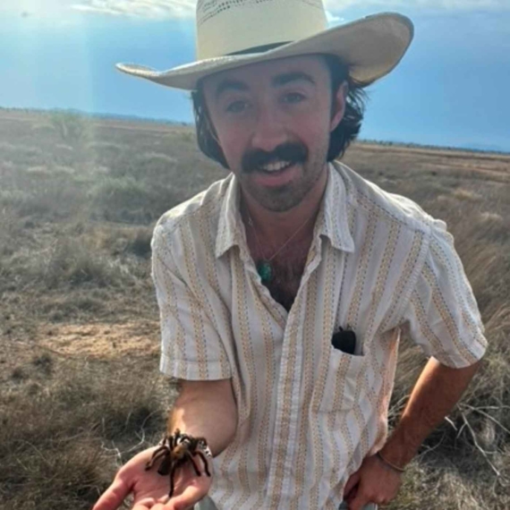 Srader outdoors, wearing a hat and holding a tarantula.